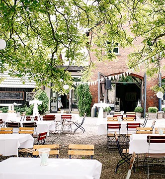 Lichtdurchfluteter Biergarten der Domäne Möllenbeck unter alten Bäumen mit eingedeckten Holztischen für Gäste