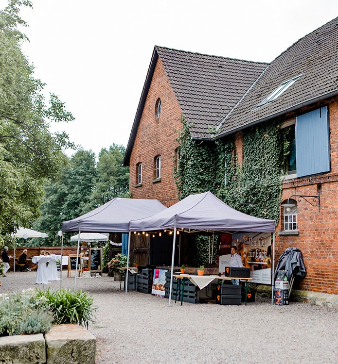 Historisches Fachwerk-Ensemble der Domäne Möllenbeck an einem sonnigen Tag, mit weißen Empfangs-Pavillons auf dem Hof